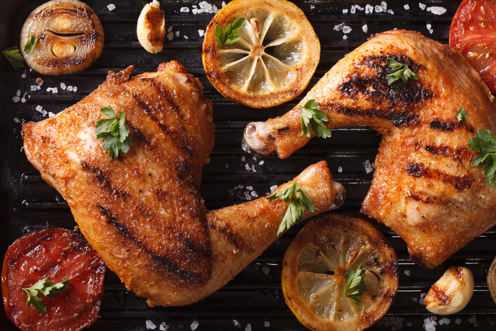 Image de morceaux de poulet rôti garnis de tranches de citron, de tomates et d’oignons grillés dans une assiette de service