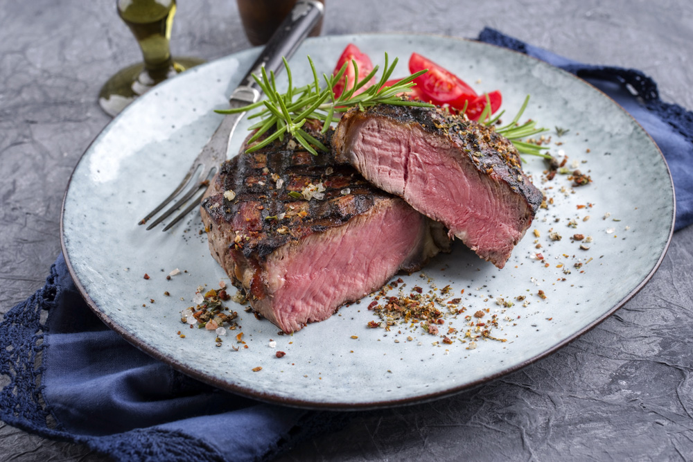 Photo d’un steak de bison mi saignant garni de romarin frais servi dans une assiette en céramique